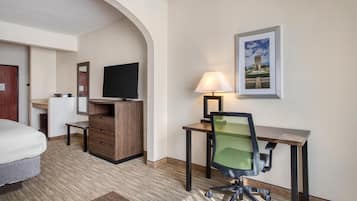 Habitación de hotel con cama, escritorio con silla, televisor, lámpara y un cuadro en la pared.