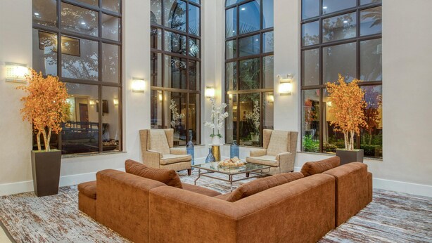 A spacious lobby with large arched windows, a brown sectional sofa, two armchairs, and a glass coffee table. - Best Western Champions Forest Inn and Suites (Houston)