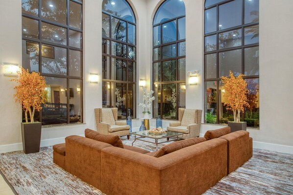 Un hallo amplio con ventanas arqueadas y un sofá seccional marrón, dos sillones y una mesa de centro de vidrio.
