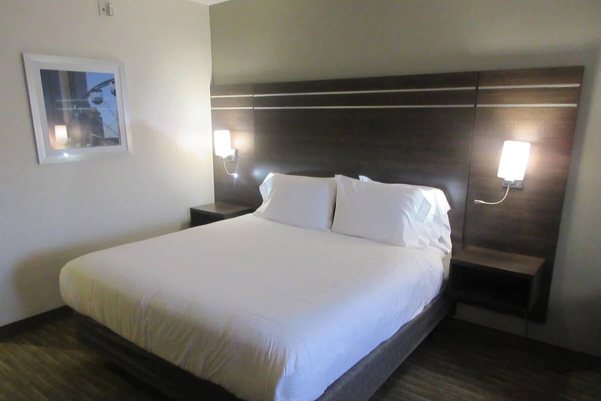 A neatly made bed with white linens, a dark headboard, and two bedside lamps.