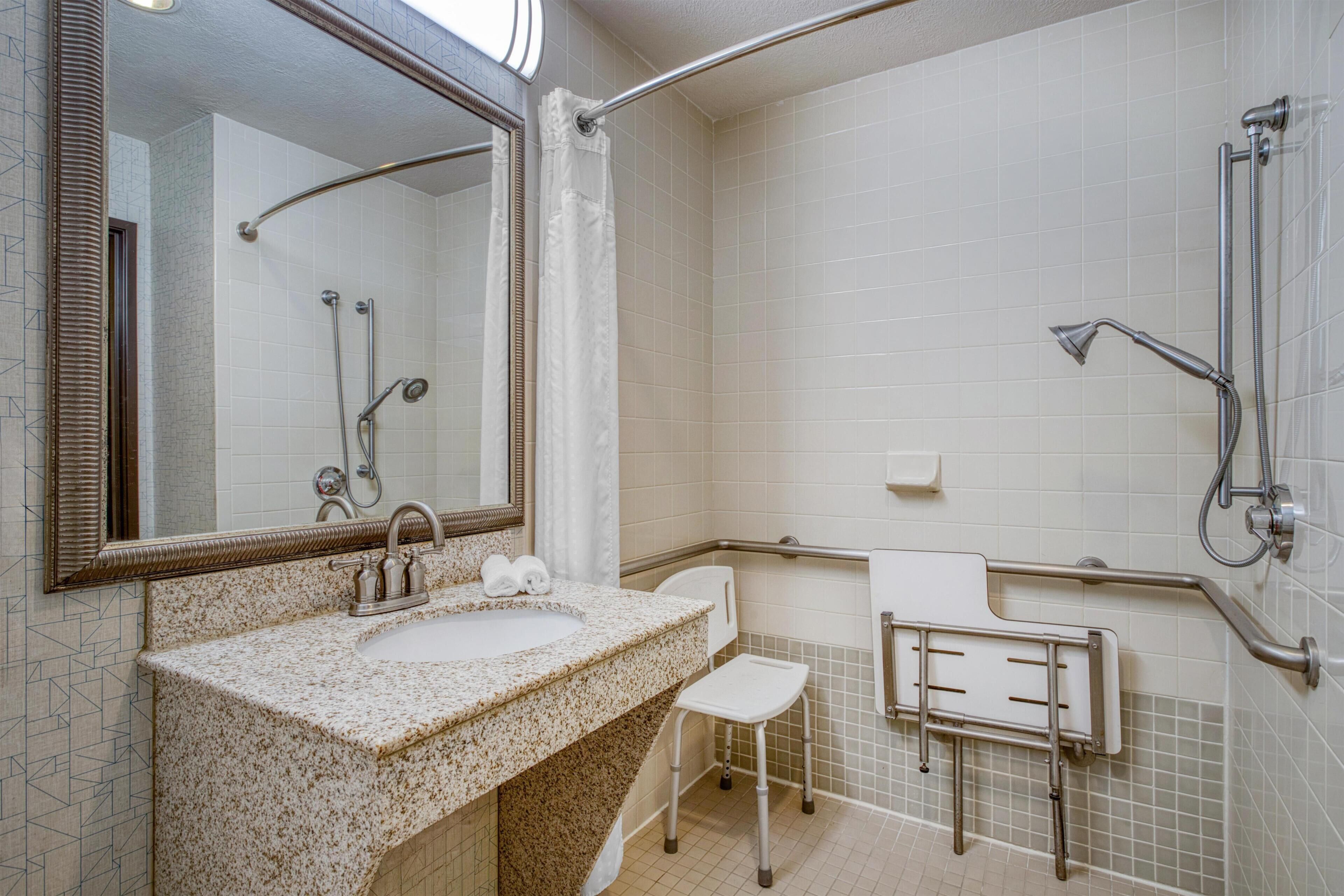 Een badkamer met een wastafel, spiegel, douche en handgrepen.