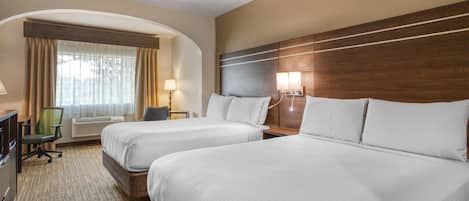 A hotel room with two beds, a desk, a chair, a lamp, and a window with curtains.