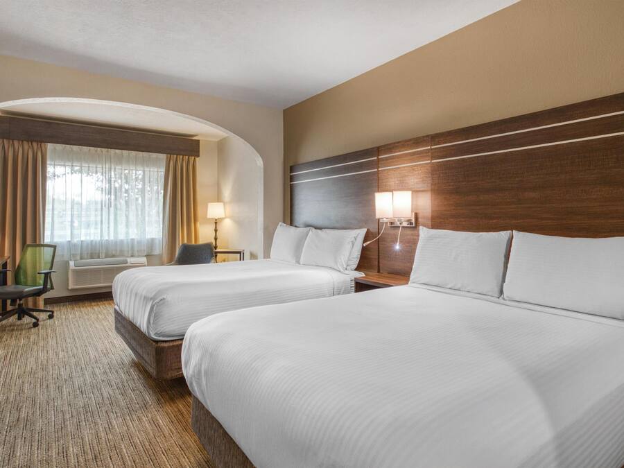 A hotel room with two beds, a desk, a chair, a lamp, and a window with curtains.