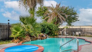 A swimming pool with a small waterfall feature, surrounded by tropical plants and a wooden fence. - Best Western Champions Forest Inn and Suites (Houston)