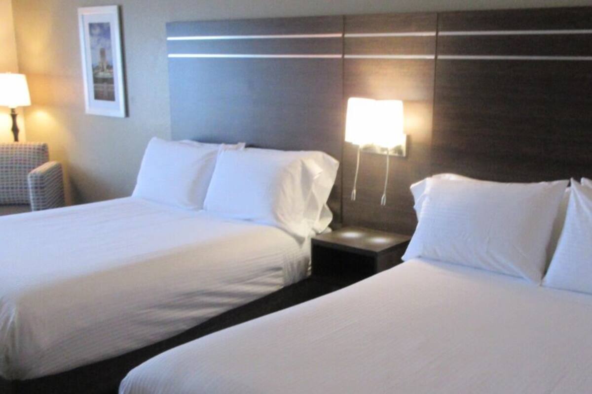 A hotel room with two beds, a nightstand, a chair, and two wall-mounted lamps.