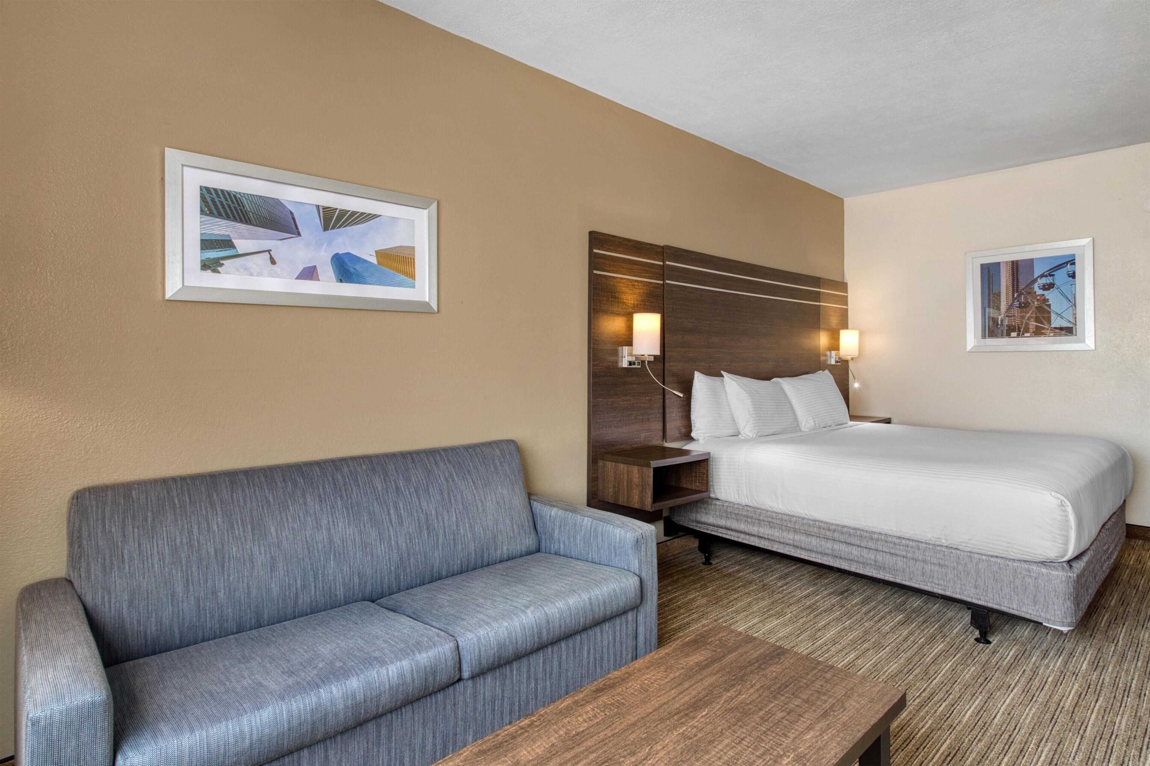 A hotel room with a bed, a sofa, a wooden nightstand, and two wall-mounted lamps.