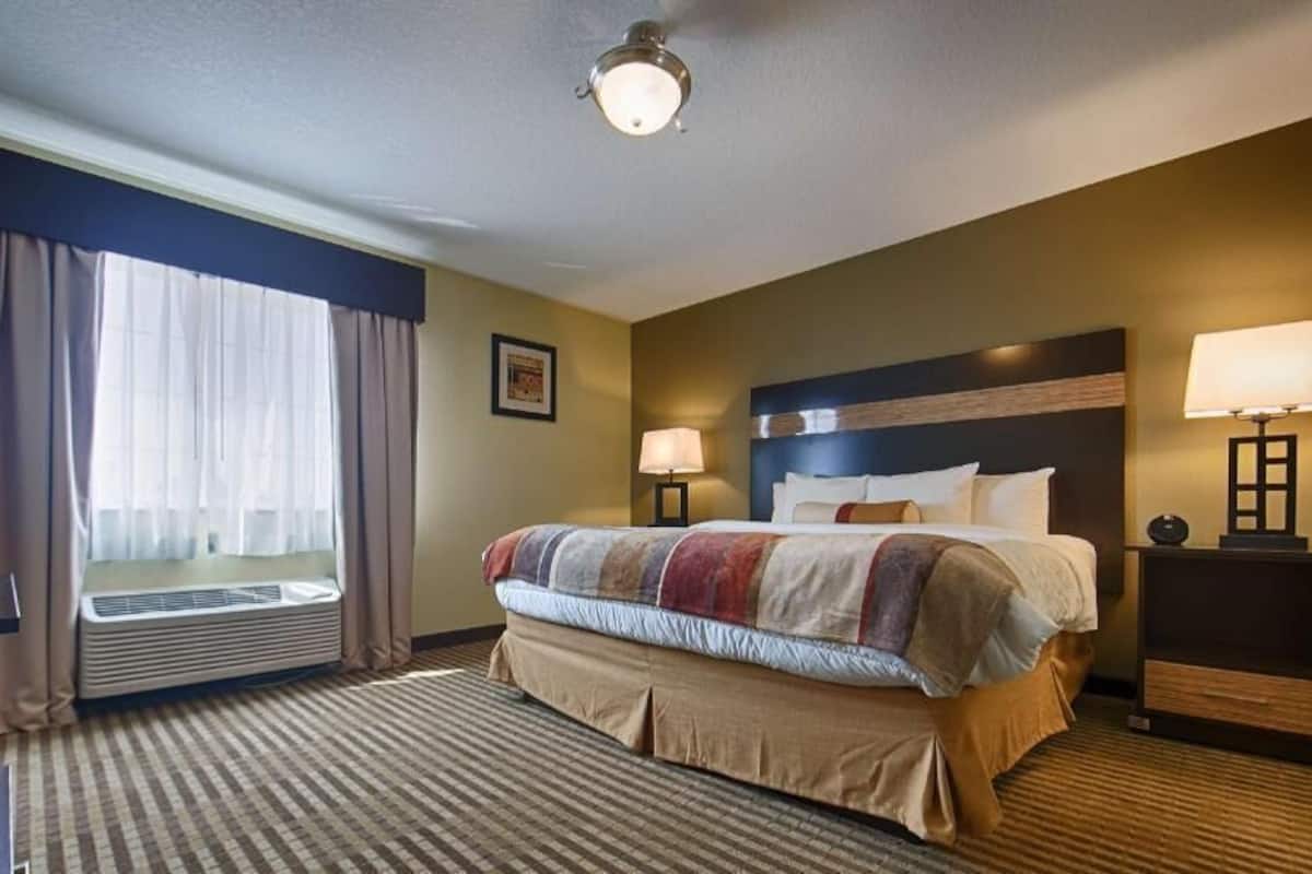 A hotel room with a large bed, two bedside tables with lamps, a window with curtains, and a ceiling light.
