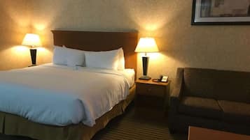 A hotel room with a bed, two bedside lamps, a nightstand with a phone, and a couch.