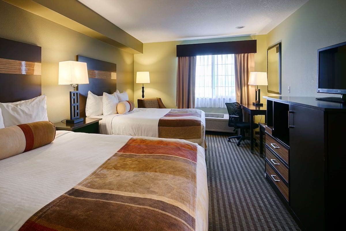A hotel room with two beds, a desk, a television, and a window with curtains.
