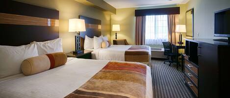 A hotel room with two beds, a desk, a television, and a window with curtains.