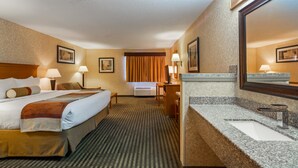 A hotel room with a bed, bedside tables, a desk, a chair, a desk lamp, a mirror, and a bathroom with a sink and mirror. - Best Western Rama Inn (Ephrata)