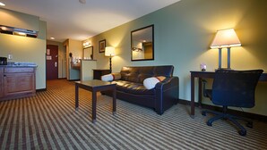 A hotel room with a sofa, a desk, a chair, a lamp, a mirror, and a kitchenette. - Best Western Rama Inn (Ephrata)