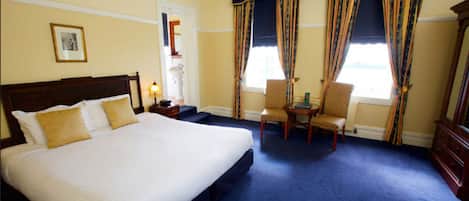 A hotel room with a large bed, two chairs, a small table, and a window with curtains.