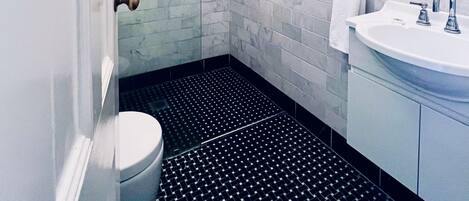 A modern bathroom with a glass shower enclosure, a white toilet, a black tiled floor, and a white sink with a mirror above it.