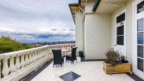A balcony with a table and chairs, a potted plant, and a view of distant buildings. - The Carrington Hotel (Katoomba)