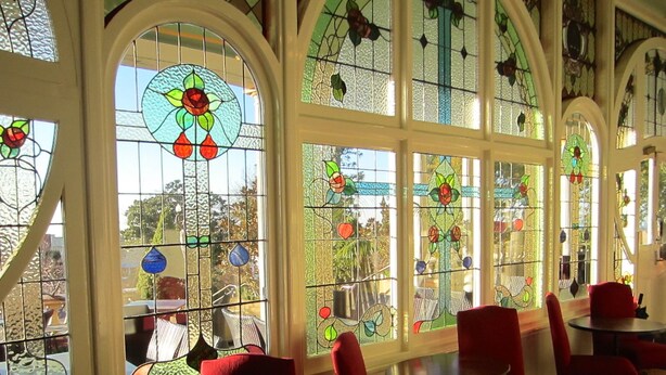 A room with large stained glass windows, red chairs, and a round table. - The Carrington Hotel (Katoomba)