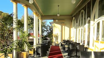 A covered outdoor seating area with tables and chairs, a red carpet, and columns.
