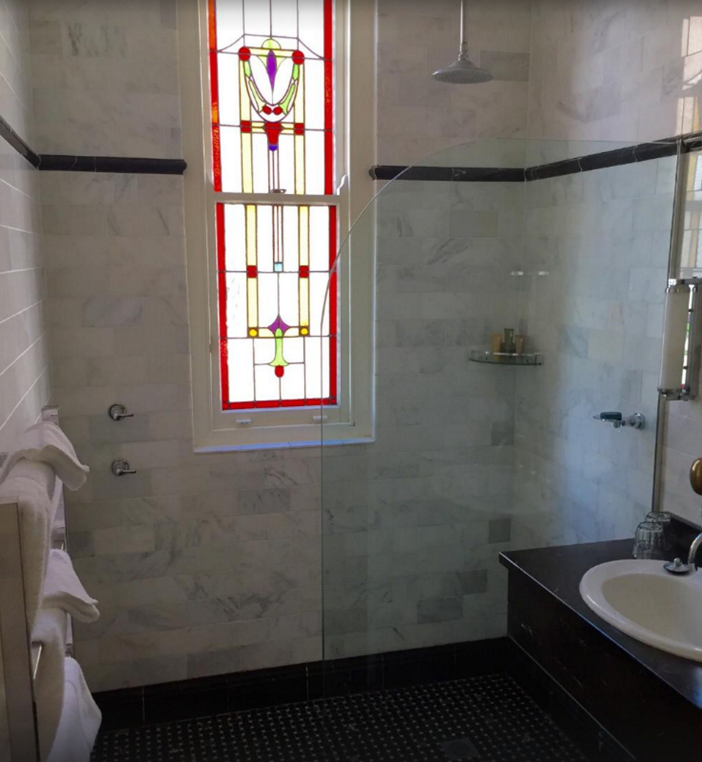 A bathroom with a glass shower enclosure, a white sink, and a stained glass window.