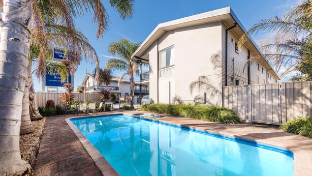 A modern building with a swimming pool, palm trees, and a fenced patio area.