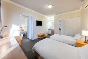 A hotel room with two beds, a desk, a TV, a small kitchenette, and a bathroom.
