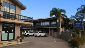 A building with a sign reading 'Best Western' and 'Governor's Room,' two white SUVs parked in front, and a balcony with a railing.