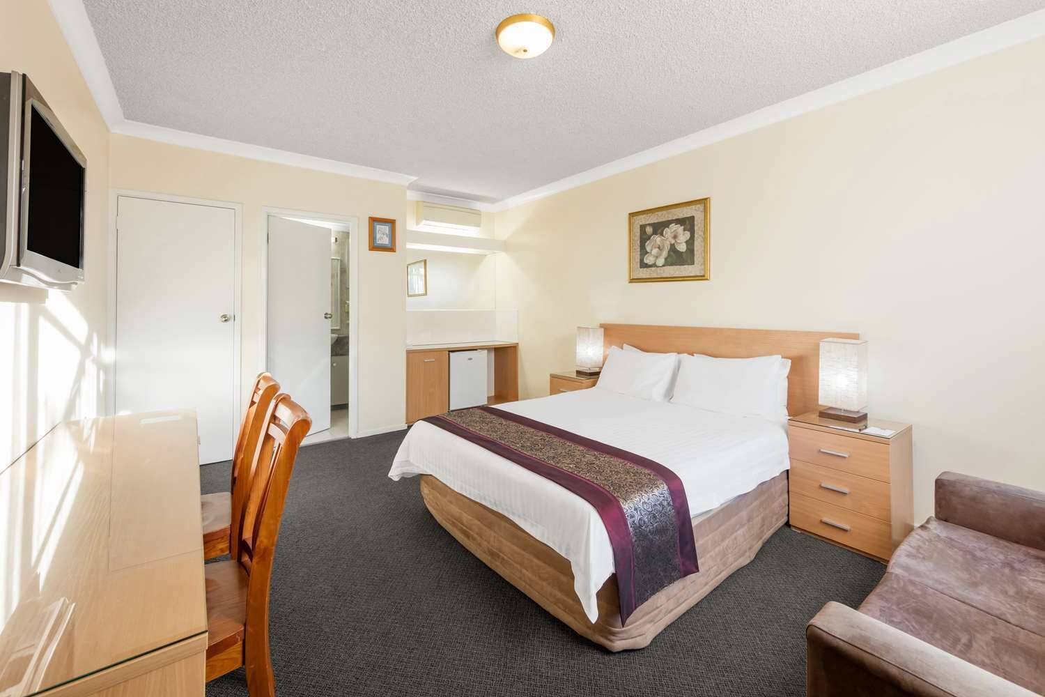 A hotel room with a bed, bedside tables, a desk, a chair, and a television.