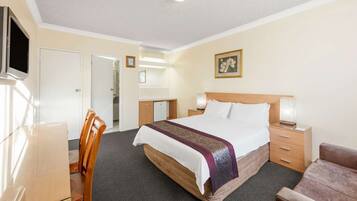 A hotel room with a bed, bedside tables, a desk, a chair, and a television.