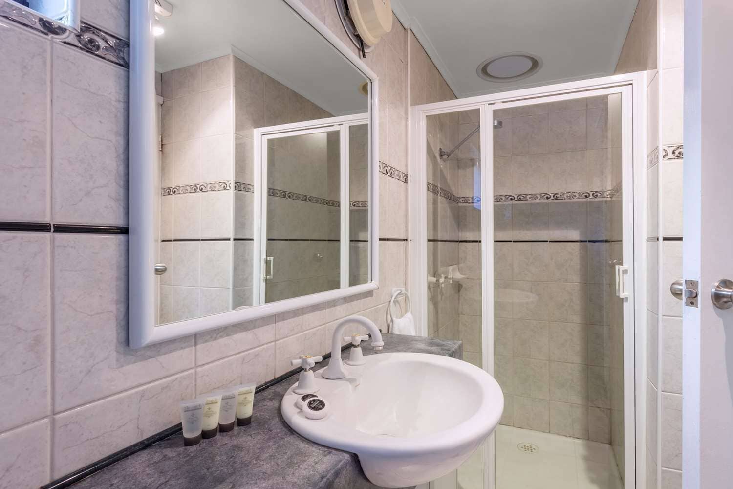 A bathroom with a sink, mirror, and shower.