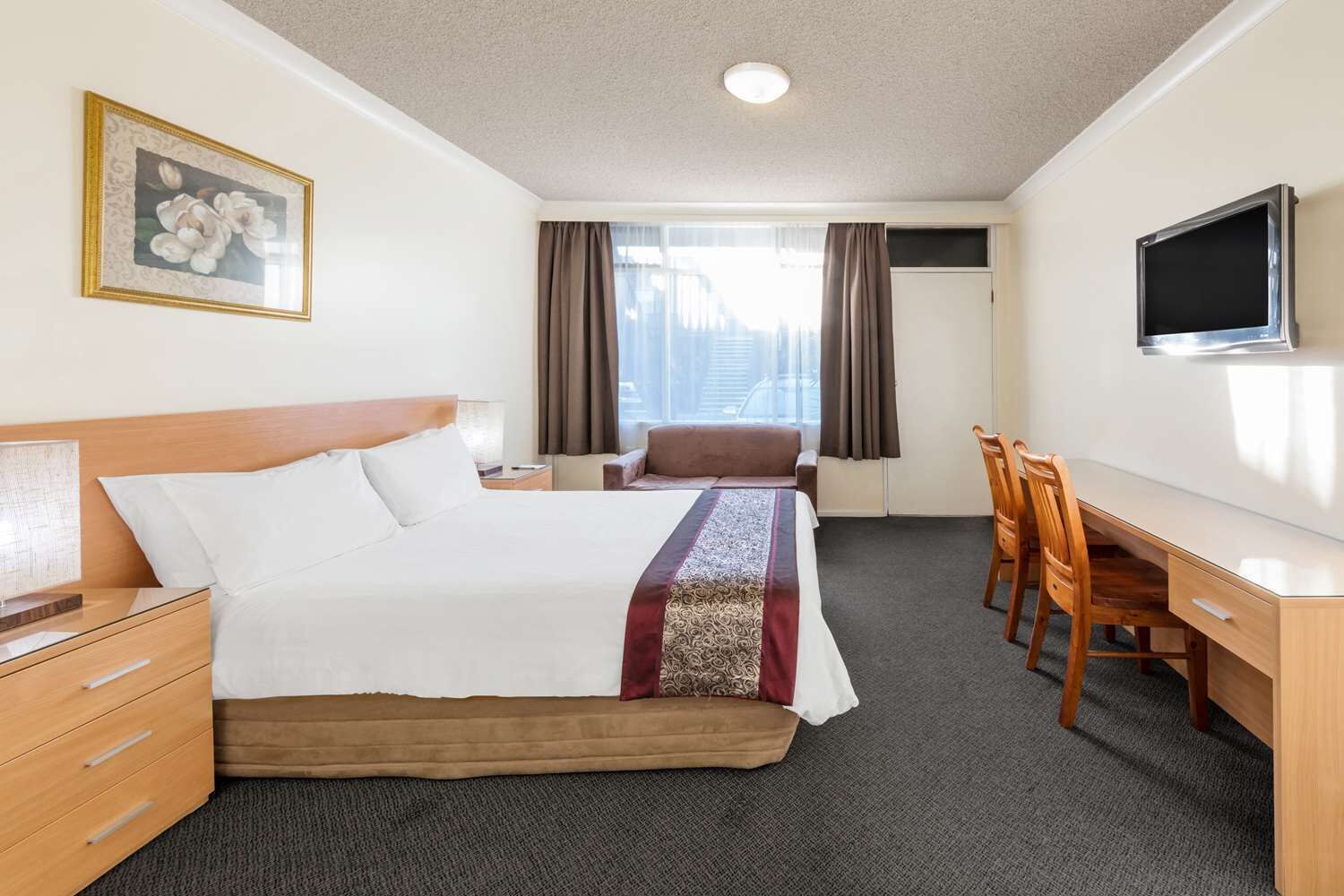 Una habitación de hotel con una cama, un escritorio, una silla, un televisor y una ventana con cortinas.