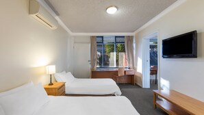 Ein Hotelzimmer mit zwei Betten, einem Schreibtisch, einem Sessel, einem Fernseher und einem Fenster mit Vorhängen.