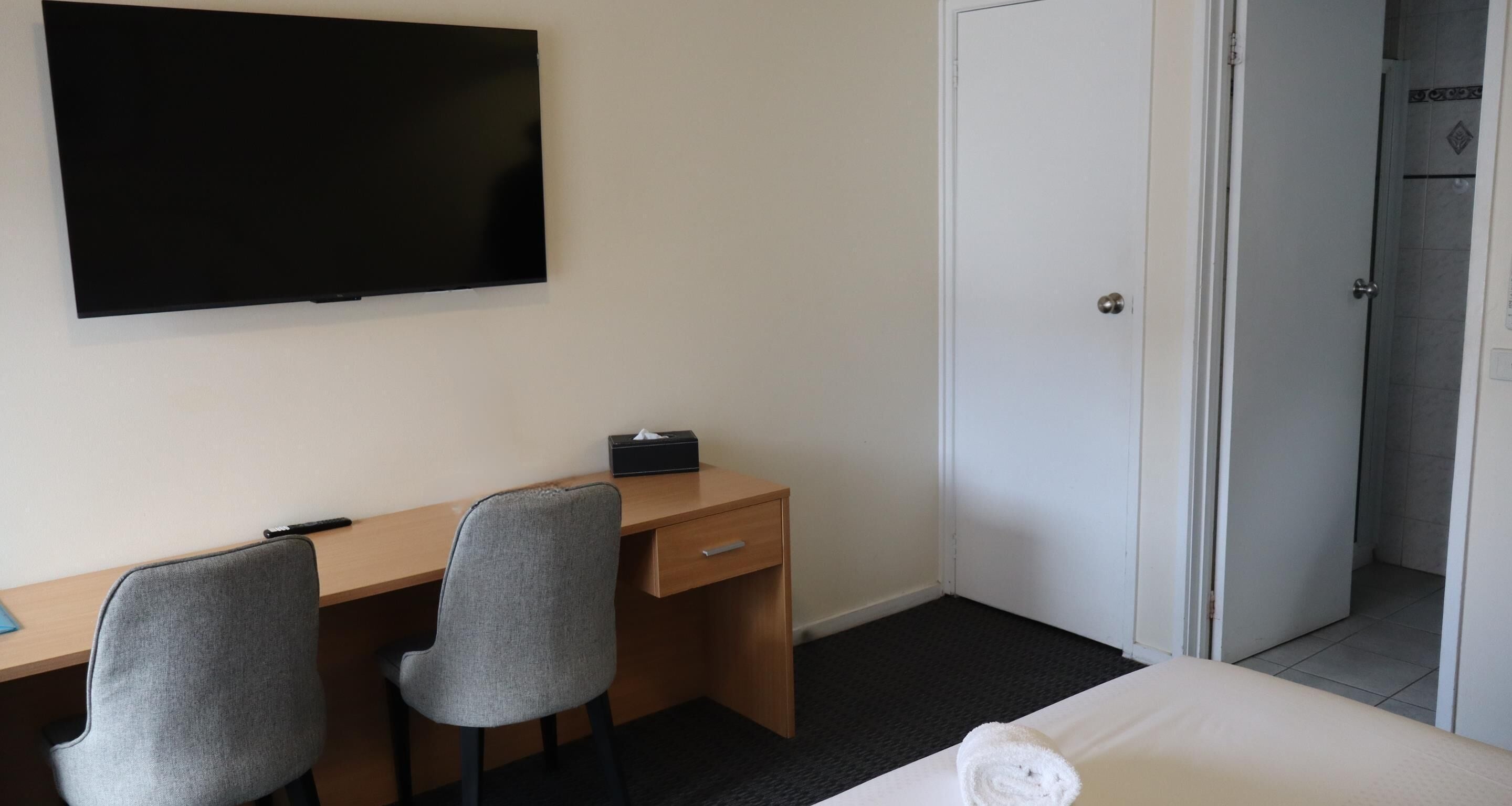 Une chambre d’hôtel comprenant un lit, un bureau avec deux chaises, une télévision et une porte donnant accès à une salle de bain.