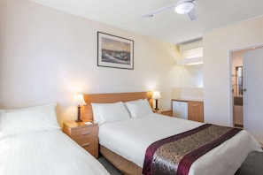 A hotel room with two beds, bedside lamps, a ceiling fan, a painting on the wall, and a door leading to a bathroom.