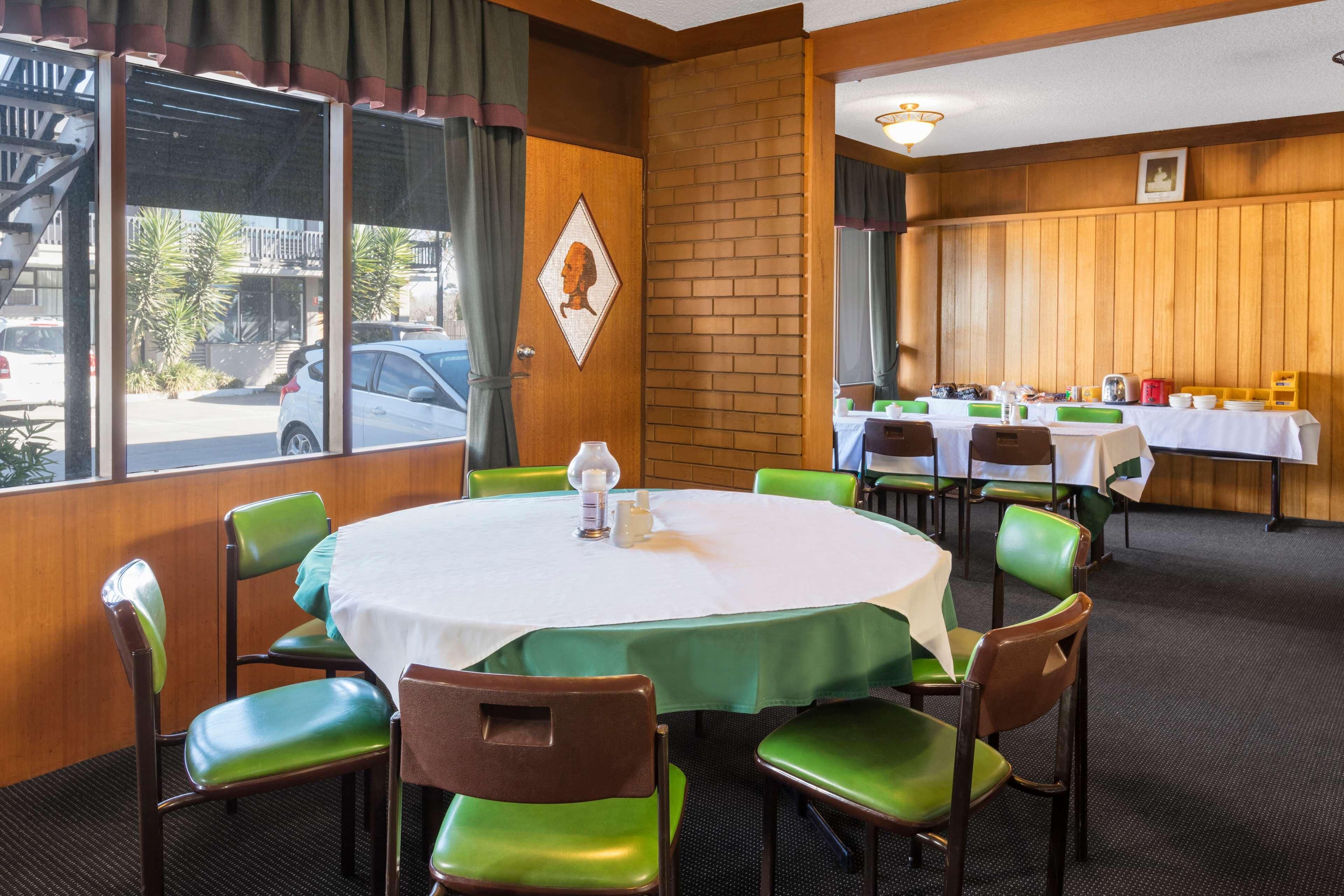 Een eetgedeelte met ronde tafels, groene stoelen en een bakstenen muur.