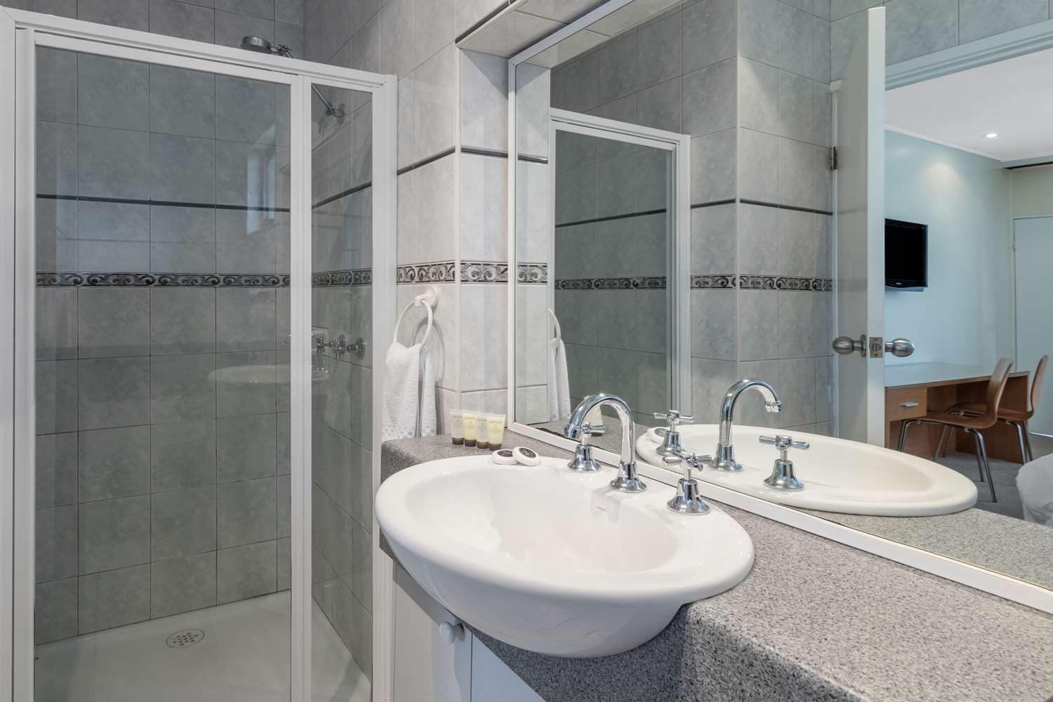 Un bagno moderno con cabina doccia, due lavandini e uno specchio grande.