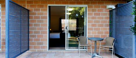 A patio with two chairs and a table, a sliding glass door leading to a room, and a brick wall.