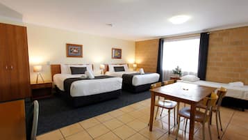 Habitación de hotel con dos camas, una mesa de comedor, sillas, una mesita con lámpara y un armario.