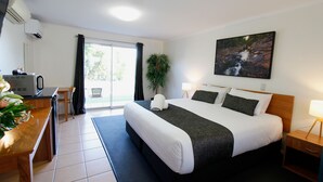 A hotel room with a large bed, a desk with a computer, a chair, a plant, and a painting on the wall. - Windmill Motel and Events Centre (Mount Pleasant)
