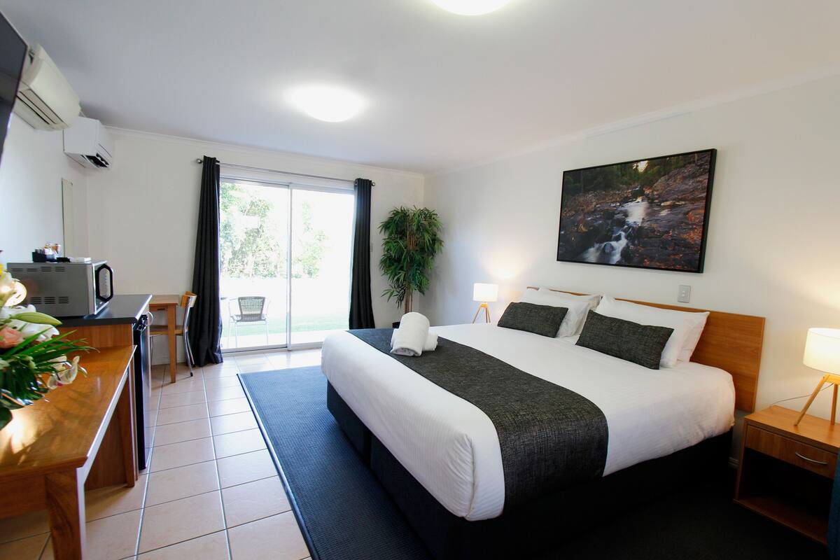 Une chambre d’hôtel avec un grand lit, un bureau avec un ordinateur, une chaise, une plante et un tableau au mur.