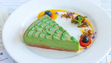 A slice of green dessert on a white plate with a grid pattern on top, accompanied by blueberries and a small dollop of cream.