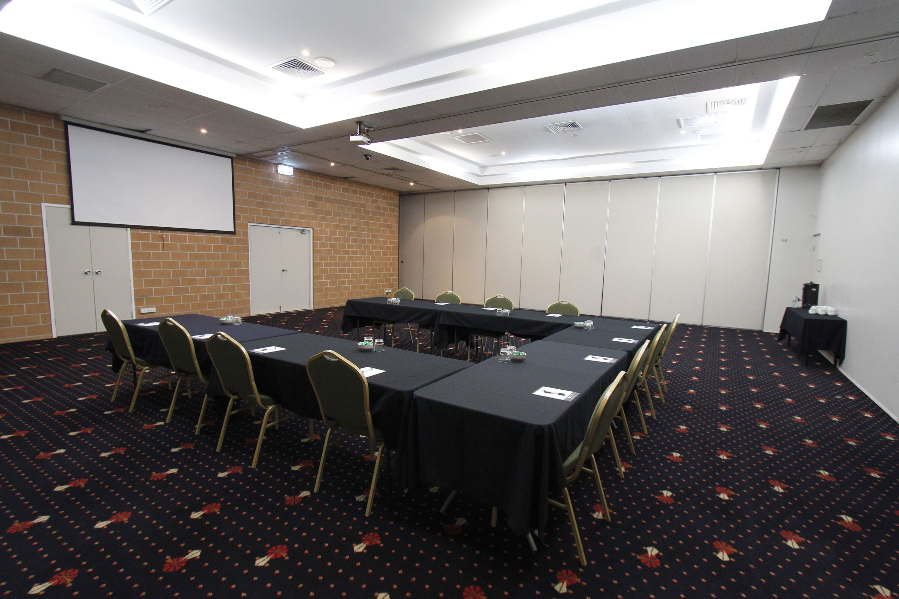 A conference room with a large table, chairs, a projector screen, and a carpeted floor.