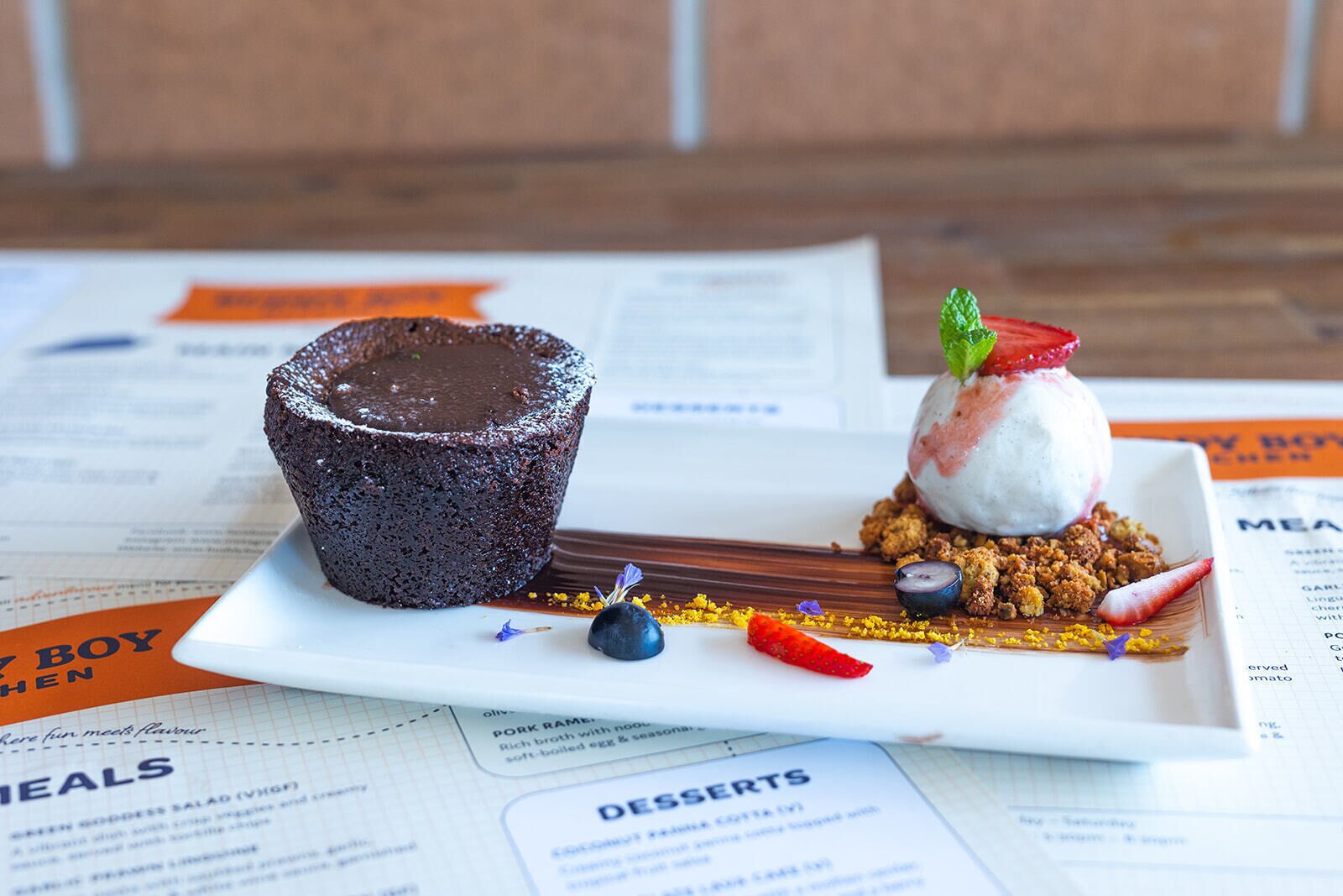 A dessert plate with a chocolate lava cake and a scoop of ice cream with fruit on top, garnished with a mint leaf.