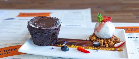 A dessert plate with a chocolate lava cake and a scoop of ice cream with fruit on top, garnished with a mint leaf.