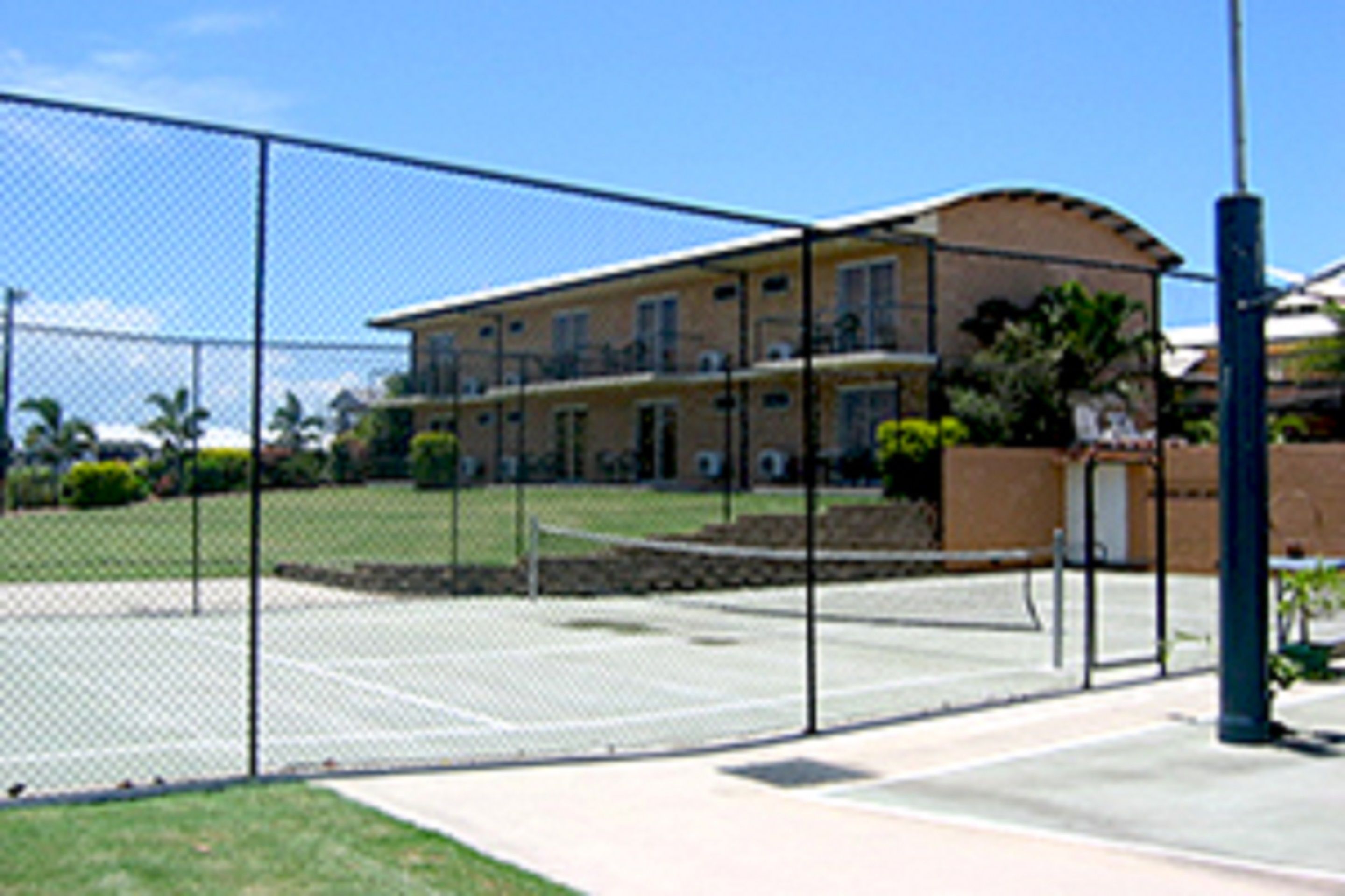 Zona de canchas de tenis con cerco y un edificio al fondo.