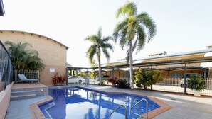 A swimming pool with a tiled deck, palm trees, and a covered walkway. - Windmill Motel and Events Centre (Mount Pleasant)