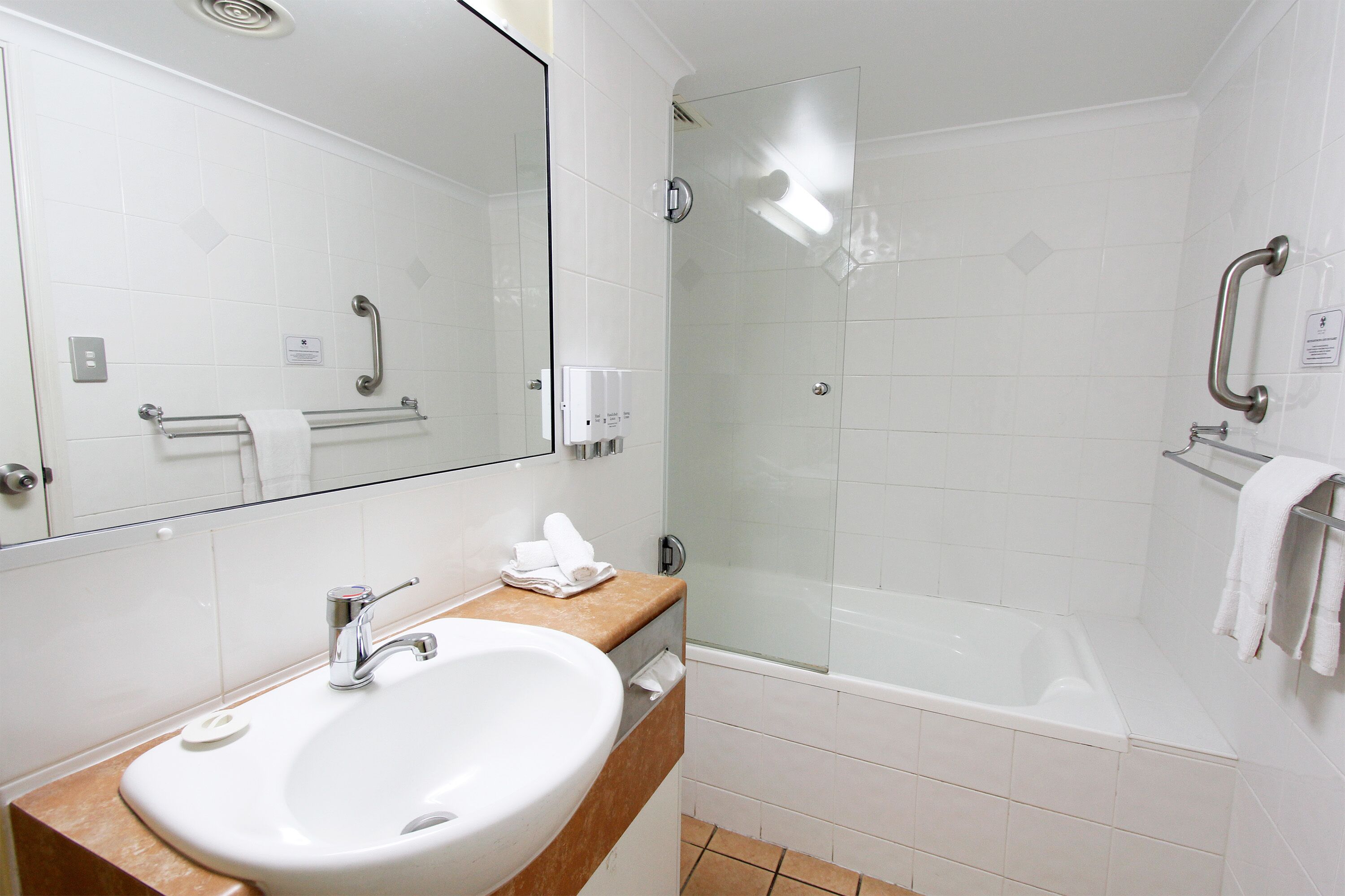 Un baño moderno con lavamanos, espejo y ducha con mampara de vidrio.