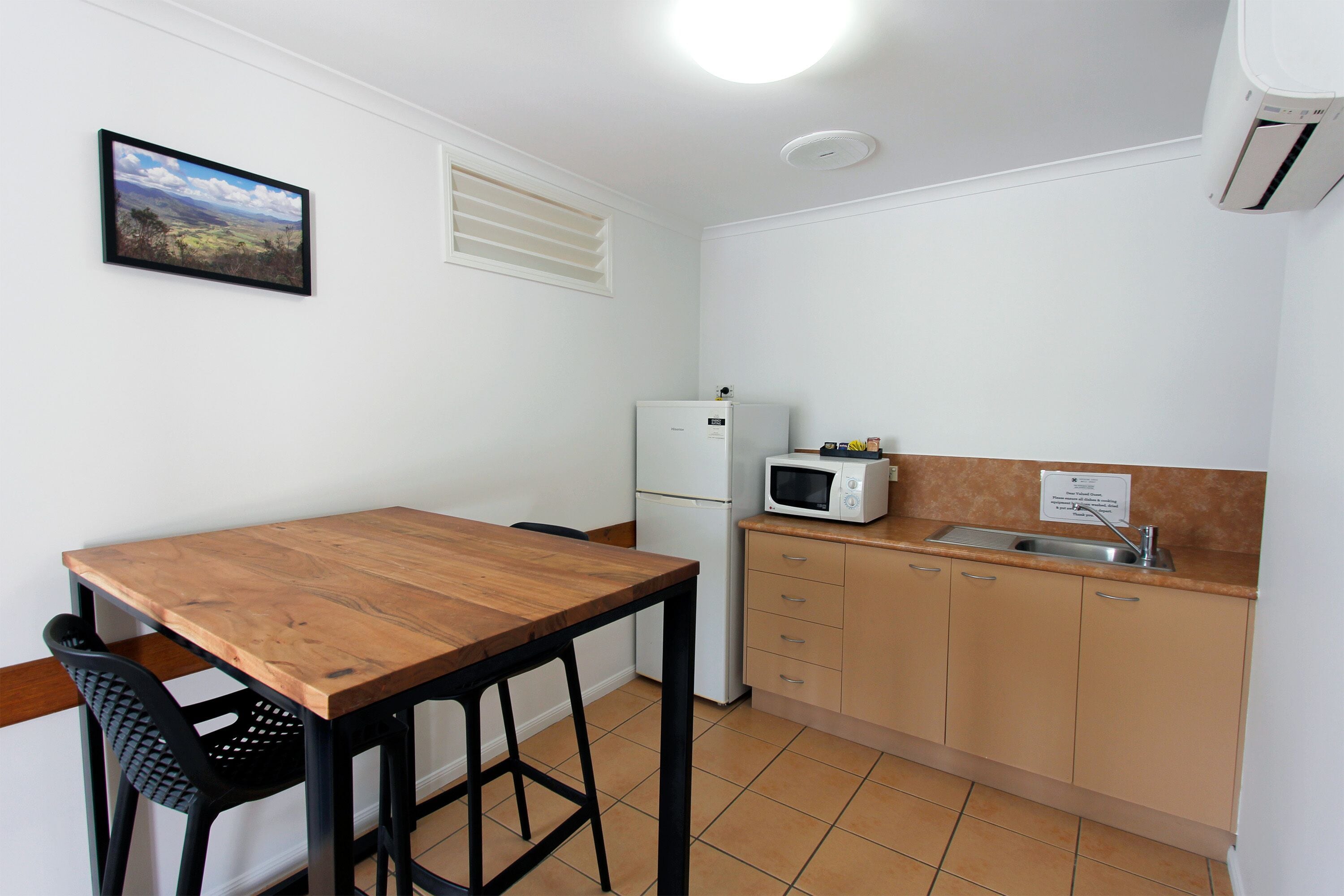Uma cozinha compacta com mesa de madeira, uma cadeira preta, geladeira branca, micro-ondas e pia.