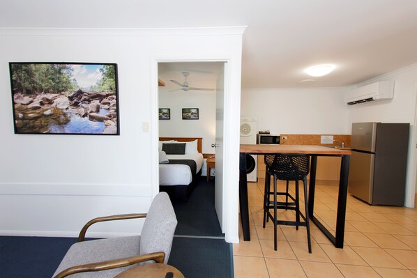 Una habitación de hotel compacta con cama, kitchenette pequeña, zona de comedor y baño.