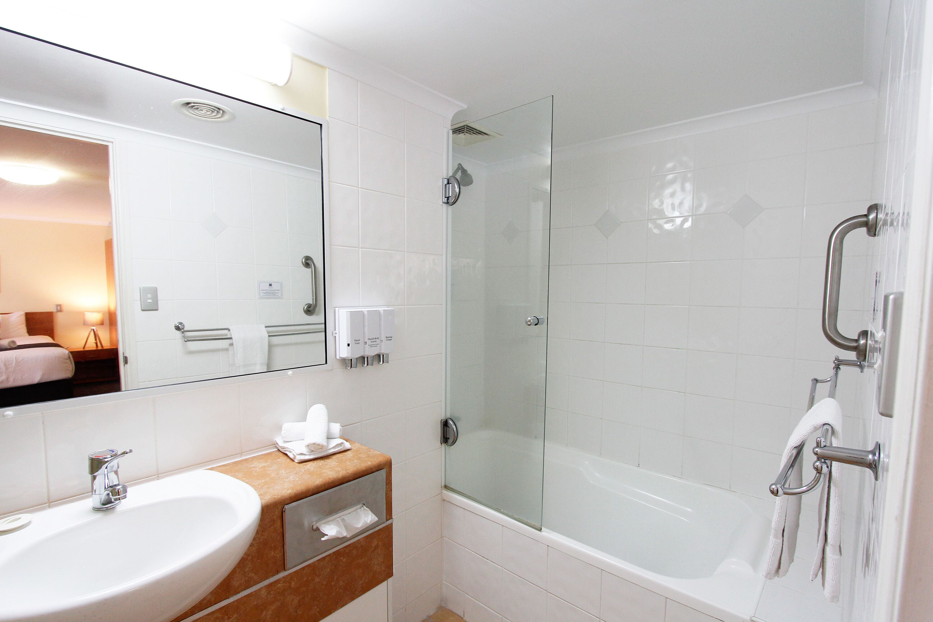 A hotel bathroom with a sink, mirror, shower, and glass door.