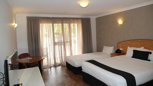 A hotel room with two beds, a desk, and a chair. There is a window with curtains, a ceiling light, and a wall-mounted phone.