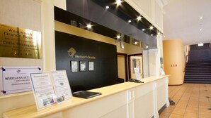 A reception desk with a black backdrop and framed pictures. There is a sign for Wentworth Grande Resort and a notice about wireless internet.